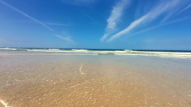 Yumuşak kum, yumuşak dalgalar, parlak mavi bir gökyüzünün yanında hoş ve huzurlu bir sahil sahnesi.