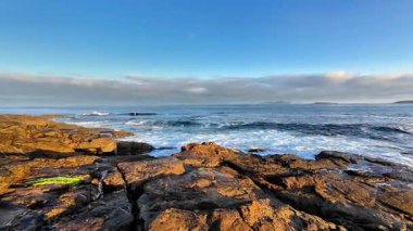 Muhteşem okyanus dalgalarının berrak bir gökyüzünün altında kayalık kıyılara çarpmasının çarpıcı ve resimsel bir görüntüsü.