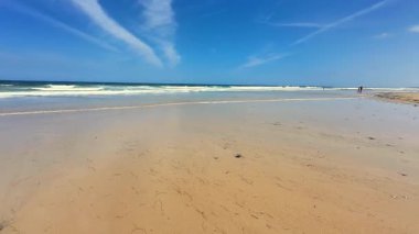 Yumuşak, sıcak kum, nazik, dingin dalgalar ve berrak mavi gökyüzünü gösteren sakin bir sahil sahnesi.