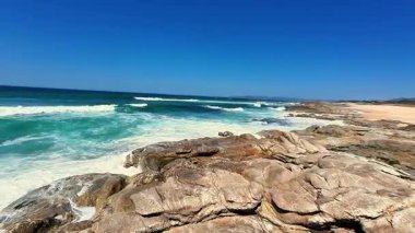 Engebeli kayalık sahilin şaşırtıcı güzellikteki manzarasında berrak mavi gökyüzü ve okyanus dalgaları çarpışıyor.