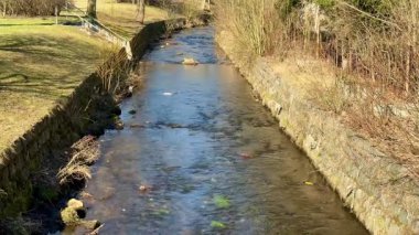 Sakin bir dere, sakin su ve canlı yeşillik içeren güzel bir arazide yavaşça akar.