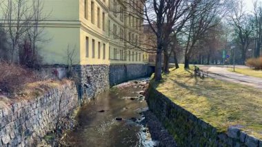 Huzurlu bir dere, güzel tasarlanmış tarihi bir binanın yanında usulca kıvrılır, canlı doğayla kucaklaşır.