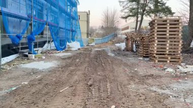 Bir inşaat alanındaki çakıllı patikada paletler ve mavi koruyucu ağ belirgin bir görünüm sergiler