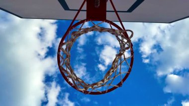Pahalı bulutlarla dolu mavi gökyüzüne karşı ayakta duran basketbol potasının canlı ve renkli bir görüntüsü.