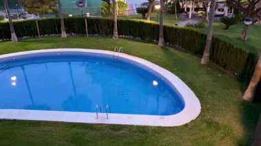 Güzel, sakin bir yüzme havuzu. Manikürlü çimenler ve palmiyelerle çevrili. Huzurlu bir yere kurulmuş.