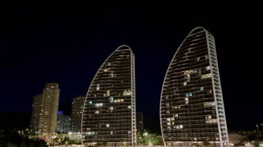 Huzurlu sahildeki gece gökyüzüne karşı görkemli bir şekilde yükselen aydınlık kulelerin muhteşem manzarasının tadını çıkarın.