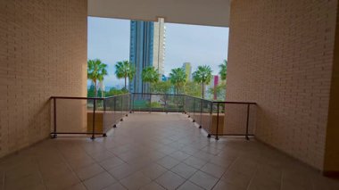 Palmiye ağaçları, bir havuz ve canlı şehir ortamında modern mimarinin yer aldığı güzel bir balkon manzarası.