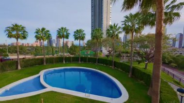 Şehir ortamında yüksek binalar ve bereketli palmiyelerle çevrili çarpıcı bir havuz manzarasının keyfini çıkardığınızı hayal edin.