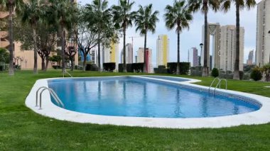 Güzel bir havuz, şehir siluetinin yanında yüksek palmiye ağaçları ile çevrilidir ve sakin bir vaha oluşturur.