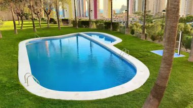 Yeşillik ve modern binalarla çevrili bir yüzme havuzunun çok güzel bir manzarası.