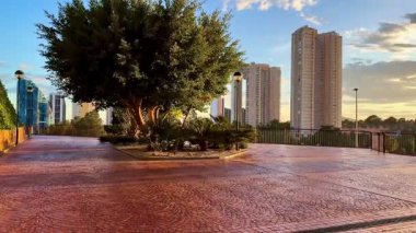 Gün batımında güzel, sakin bir şehir parkı sahnesi. Canlı yeşil binaların yanında çarpıcı modern binalar.