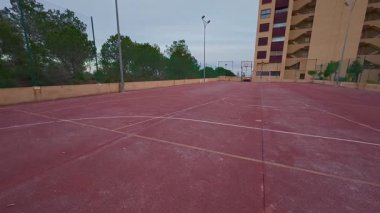 Bereketli yeşilliklerin ve yakınlardaki yerleşim alanlarının ortasındaki canlı kırmızı basketbol sahasının huzurlu manzarası