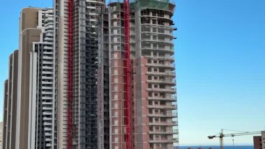 Bu canlı manzara, açık mavi gökyüzüne karşı inşaat halindeki binaları ve vinçleri gösteriyor.