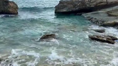 Huzurlu bir sahil sahnesi güzel bir şekilde dalgaların ritmik bir şekilde kayalara çarptığını gösteriyor.