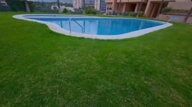 Huzurlu bir yüzme havuzu, modern bir yerleşim bölgesinde canlı yeşil bir çimenlikle çevrilidir.