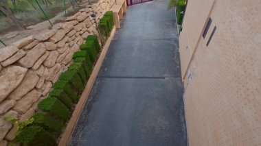 Güzel tasarlanmış modern bir yol, yemyeşil yapraklar ve büyüleyici taş duvarlarla çevrili güvenli bir kapıya götürür.