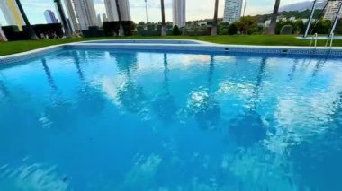 Gökyüzünü ve gökdelenleri yansıtan bir havuz, rahatlama ve yaz atmosferi için mükemmel bir ortam yaratıyor.