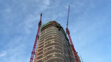 Nefes kesici bir manzara inşaat halindeki görkemli bir gökdeleni ve açık mavi gökyüzünün altında hareketli vinçleri gösteriyor.