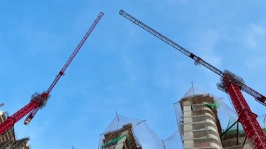 Dinamik bir inşaat sahasında çeşitli vinçler sergileniyor. Etkileyici modern yapılar üzerinde özenle çalışıyorlar.