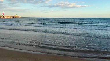 Yumuşak dalgaların sakin ve pitoresk bir görüntüsü berrak bir gökyüzünün altındaki kumlu kıyıya hafifçe çarpıyor