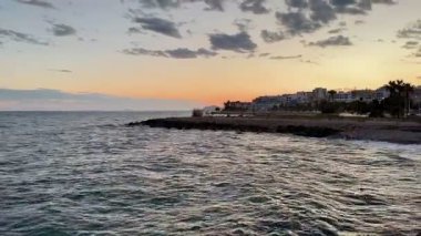 Göz kamaştırıcı bir günbatımı huzurlu ve manzaralı bir sahil şeridinin huzurlu sularında canlı renkler bırakır.