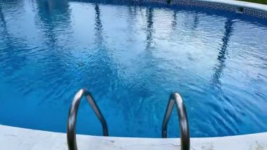 Zarif palmiye ağaçları, şehir arkaplanı ve sakin, davetkar mavi sular içeren sakin bir havuz manzarası yaşayın.