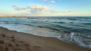 Gün batımında kumlu sahile yuvarlanan yumuşak dalgaların dingin güzelliğine dalın.