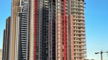 İnşaat halindeki yüksek binaların göz kamaştırıcı görüntüleri, açık mavi gökyüzüne karşı vinçler.