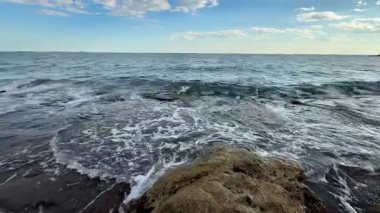 Açık ve aydınlık bir günde, dingin okyanus dalgaları güçlü kayalara karşı ritmik bir şekilde yıkanıyor.