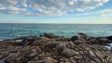 Üzerinde yumuşak, bulutlu bir gökyüzü altında kayalık çıkıntılar barındıran güzel, sakin bir kıyı manzarası.
