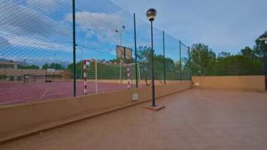 Yeşillik ve ağaçlarla çevrili bir basketbol sahasının olduğu canlı bir spor alanı.