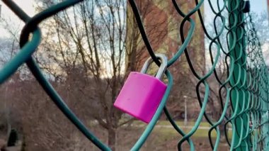 Parlak ve canlı pembe bir asma kilit sağlam bir tel örgüye bağlanır, sakin bir zemin üzerine kurulur.