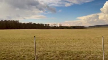 Pofuduk, dağınık bulutlarla benekli, parlak mavi gökyüzünün altında geniş alanlar gösteren huzurlu bir manzara.