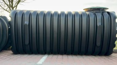 Güçlü bir siyah depolama tankı, tarım veya endüstriyel kullanım için ideal, dayanıklı kaldırım taşlarının üzerinde bulunur.