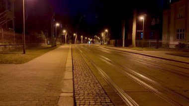 Geceleri sokak lambalarıyla aydınlatılan tramvay raylarının yer aldığı sakin ve huzurlu bir şehir manzarası.