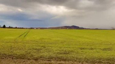 Canlı ve canlı yeşil bir alan, kasvetli bir gökyüzünün altındaki uzak, yuvarlanan tepelere doğru zarif bir şekilde uzanıyor.