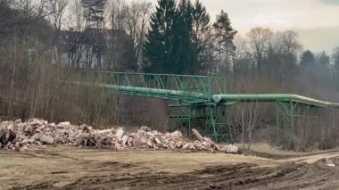 Endüstriyel alan boyunca uzanan uzun yeşil bir konveyör köprüsü ön planda çeşitli enkaz parçalarıyla birlikte...