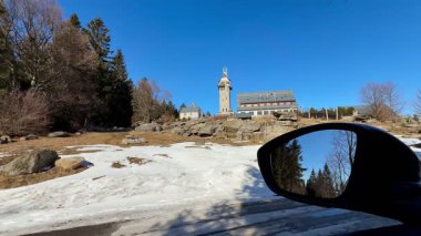Beyaz kar ve açık mavi gökyüzü ile çevrili tarihi bir kule ve büyüleyici bir otel manzarası görüyorsunuz.