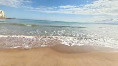 Yumuşak altın kumu, yumuşak dalgaları ve çarpıcı açık mavi gökyüzünü gösteren sakin bir sahil manzarası hayal edin.