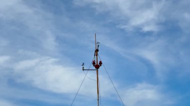 Kendini işine adamış bir işçi, açık mavi gökyüzünün altında yüksek bir iletişim kulesinin tepesinde hayati önem taşıyan bakımı yaparken görülebilir.