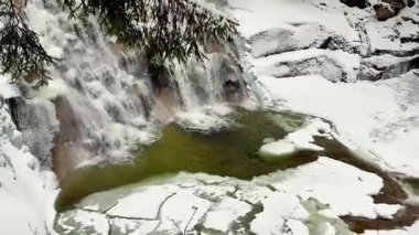 Parlak kar ve buzla çevrili güzel çağlayan bir şelalenin yer aldığı pitoresk bir kış sahnesi hayal edin.