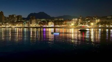 Gece güzelce aydınlatılan, sakin suları yansıtan canlı deniz kenti nefes kesici bir manzara.