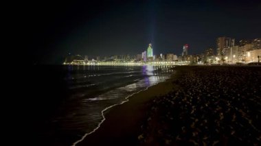 Geceleri huzurlu ve huzurlu bir sahil manzarası şehrin ışıklarını ve okyanus yansımalarını güzel bir şekilde gösteriyor.
