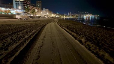 Gece şehir ışıklarıyla aydınlatılmış sakin bir sahil yolu, rahatlama ve sükunet için mükemmel..