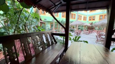 Açık hava oturma alanı büyüleyici bir restoranda canlı yeşillikler arasında şık ahşap mobilyalar barındırır.