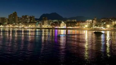 Geceleri göz kamaştırıcı kentsel ufuk çizgisi durgun su yüzeyine yansıyan parlak ışıkları sergiliyor.