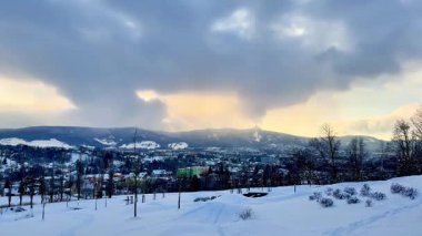 Karla kaplı tepeleri resmeden huzurlu ve sakin bir kış manzarası. Alacakaranlıkta bulutlu güzel bir gökyüzü.