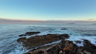 Uçsuz bucaksız okyanusun kayalık kıyılarla buluşmasını gerçekten nefes kesici bir manzara, hepsi çarpıcı bir alacakaranlık gökyüzünün altında.