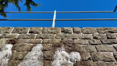 Metal parmaklıklarla süslenmiş güzel ve resimsi taş bir duvar, hepsi yukarıdaki parlak mavi gökyüzüne karşı kurulmuş.