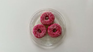 Cömertçe şeker serpiştirilmiş üç lezzetli ve canlı pembe çörek güzel bir cam tabakta şık bir şekilde servis edilir.
